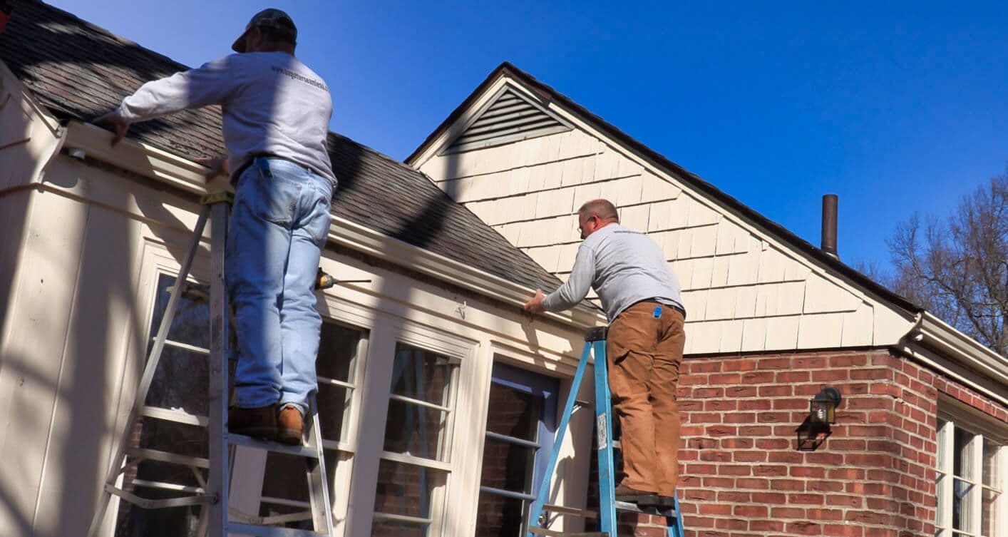 Two workers installing gutters on white-sided colonial